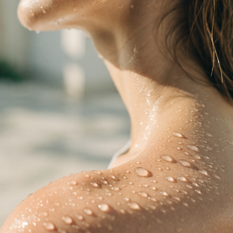 Sonnenbeschienene Schulter mit frischen Wassertropfen auf der Haut